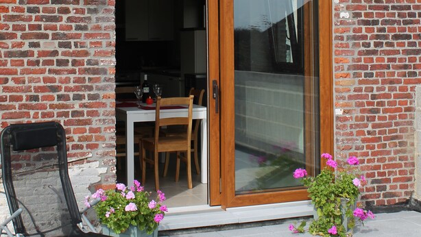 Un bâtiment en briques avec une porte et une fenêtre en bois, une chaise et des plantes en pot.