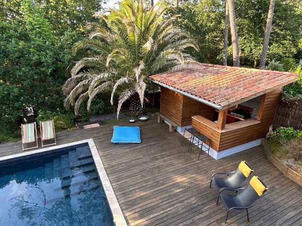 A wooden outdoor structure with a tiled roof, a pool, and seating.