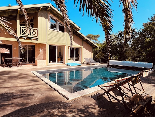 A poolside area with a pool, lounge chairs, and a building with large windows and a balcony.