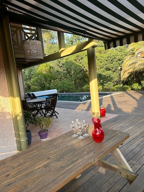 A wooden deck with a table and chairs, a hanging basket, and a red vase.