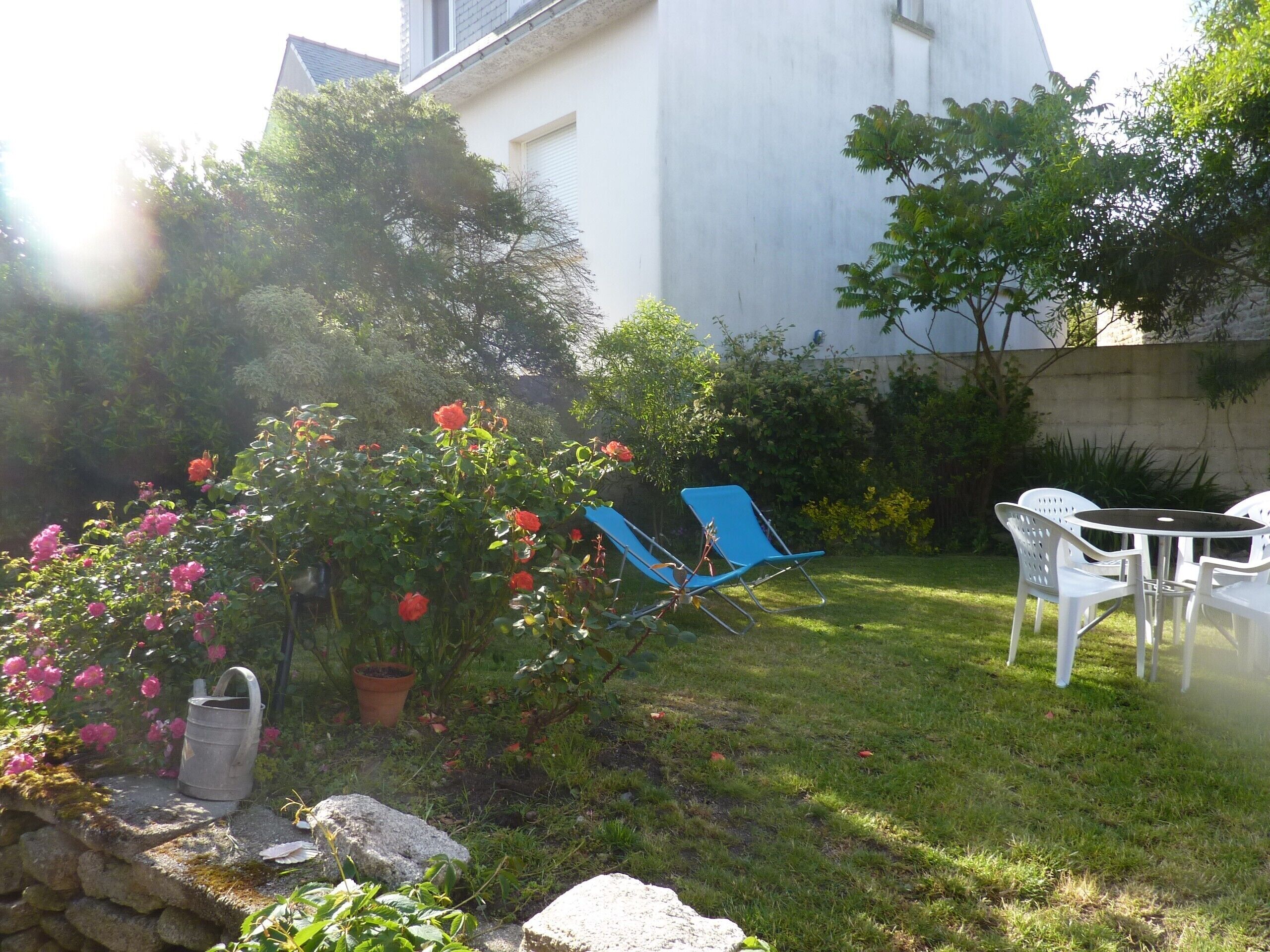 A garden with a lawn, a blue chair, a white table, and a stone wall.