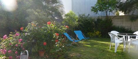 A garden with a lawn, a blue chair, a white table, and a stone wall.