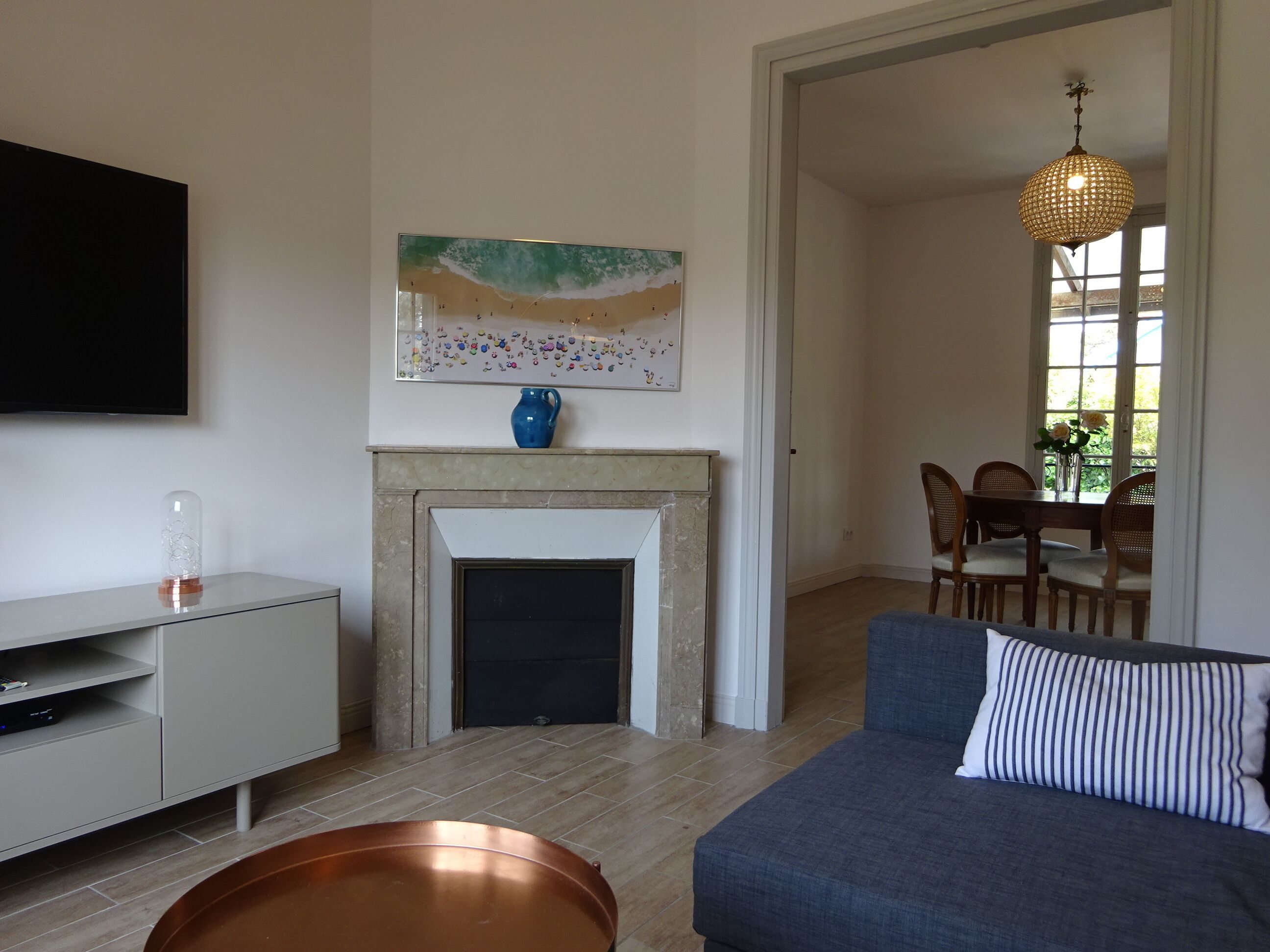 Un salon avec une cheminée, un téléviseur, un coin repas avec des chaises et un luminaire suspendu.
