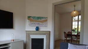 Ett vardagsrum med en öppen spis, en tv, en matplats med stolar och en hängande lampa.