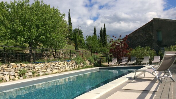 Une piscine avec des chaises longues et un mur en pierre.