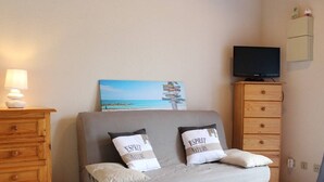Une chambre à coucher comprenant un lit, une commode en bois, un téléviseur posé sur un meuble et un meuble fixé au mur.
