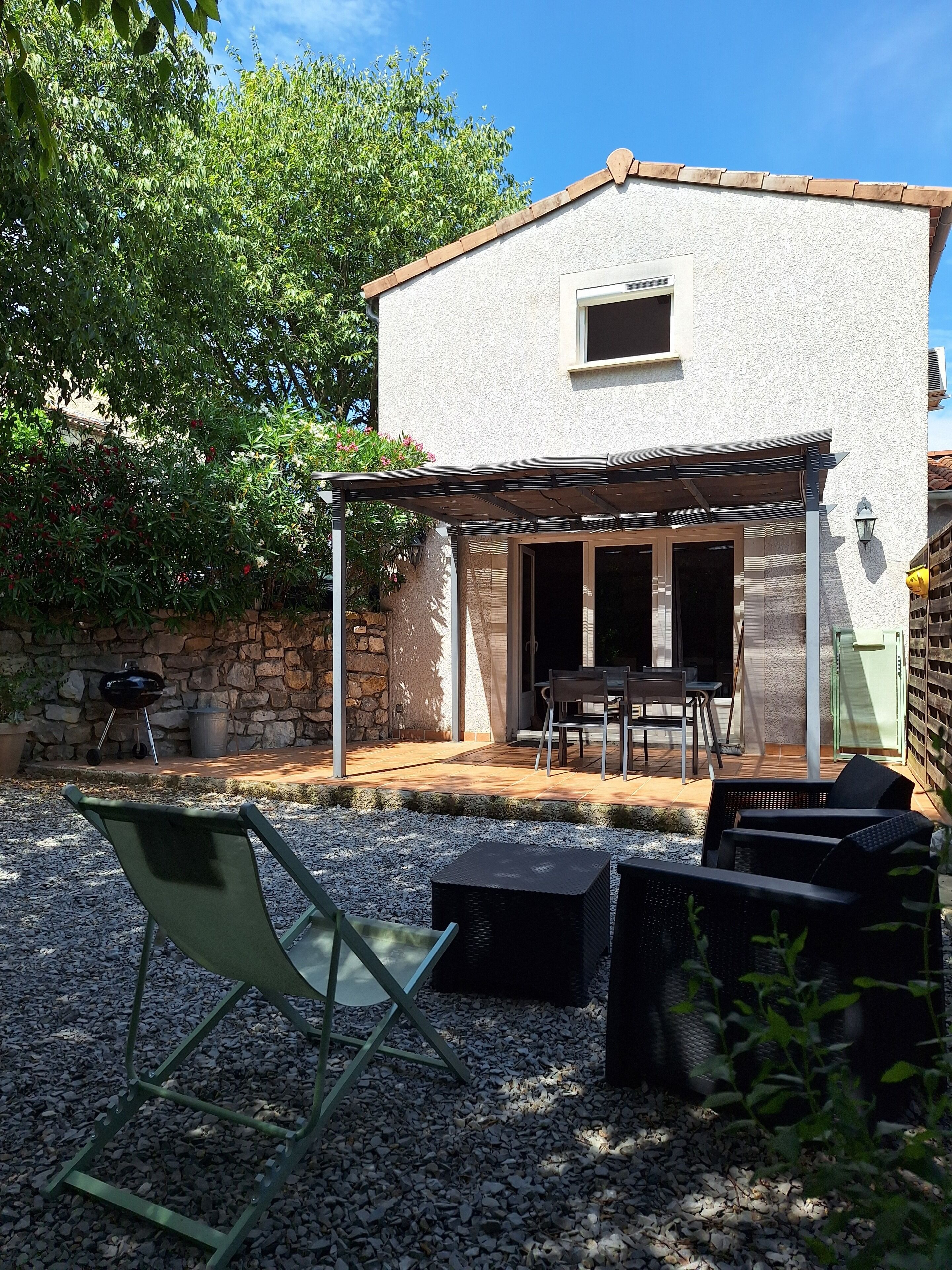 A covered patio area with outdoor furniture, a barbecue grill, and a stone wall.