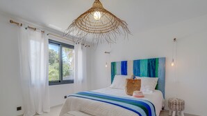 Ein Schlafzimmer mit Bett, einer Bank, einer Pendelleuchte und einem Fenster mit Vorhängen.