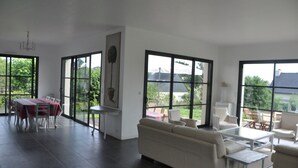 A spacious living area with a dining table and chairs, a sofa, and a coffee table. Large windows provide views of the outdoors. -  Large luxury & calm villa (4 stars), close to beaches & small sea view (Saint-Gildas-De-Rhuys)