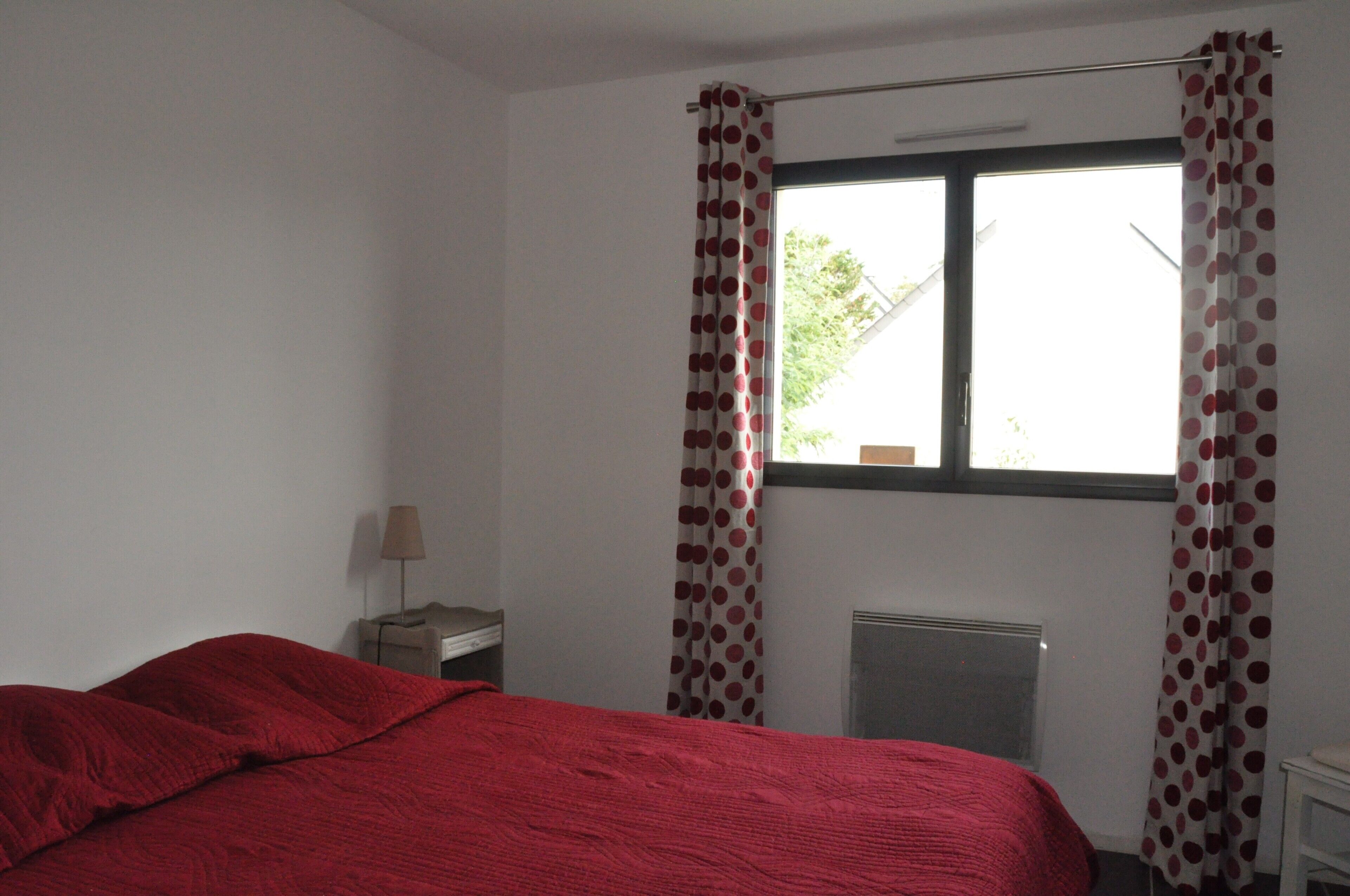 Une chambre à coucher avec un lit, un radiateur, une fenêtre avec des rideaux et une table de chevet avec une lampe.