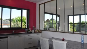 A modern kitchen with a red accent wall, large windows, and a dining area with a table and chairs. -  Large luxury & calm villa (4 stars), close to beaches & small sea view (Saint-Gildas-De-Rhuys)