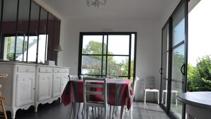 A dining area with a table set for four, white cabinets, and a view through large windows. -  Large luxury & calm villa (4 stars), close to beaches & small sea view (Saint-Gildas-De-Rhuys)