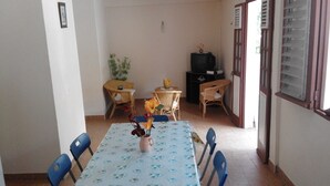 A dining area with a table set for four, surrounded by blue chairs. There is a small table with a plant and a vase with flowers in the center of the room. - APARTMENT F3 bottom of villa to rent for holidays (ANSES D'ARLET)