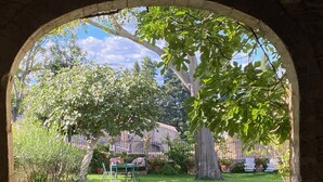 Un arco de entrada da a un jardín bien cuidado, con césped, un árbol grande y un sendero de piedra.