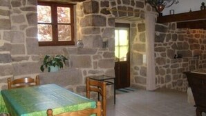 A stone-walled room with a dining table and chairs, a window, and a fireplace. - Quiet cottage with beautiful view (Chirols)