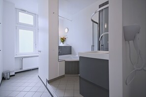 Ein modernes Badezimmer mit einem weißen Waschbecken, einem Spiegel, einer Dusche und einem an der Wand befestigten Föhn.