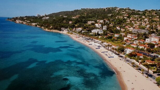 Vista aérea de un pueblo costero con playa, edificios y un paisaje montañoso.