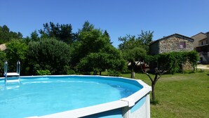 A rectangular swimming pool with a white edge, surrounded by a grassy lawn and trees.