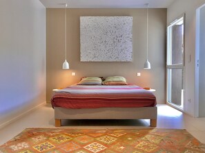 A modern bedroom with a large bed, a decorative wall piece, and a view of the outdoors.