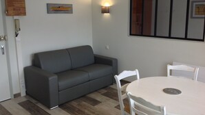 Ein modernes Wohnzimmer mit einer grauen Couch, einem weißen Esstisch mit Stühlen und einer wandmontierten Leuchte.
