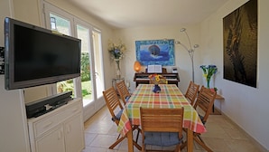Un coin repas avec une table dressée pour quatre personnes, un téléviseur, un piano et un tableau accroché au mur.