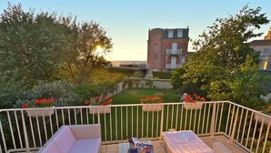 Un balcon agrémenté de meubles en osier, d’une petite table et offrant une vue sur un immeuble et un jardin.