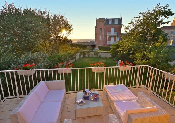 A balcony with wicker furniture, a small table, and a view of a building and garden.