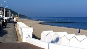 Une plage bordée de rangées de cabanes de plage blanches, un ciel dégagé et une mer calme.
