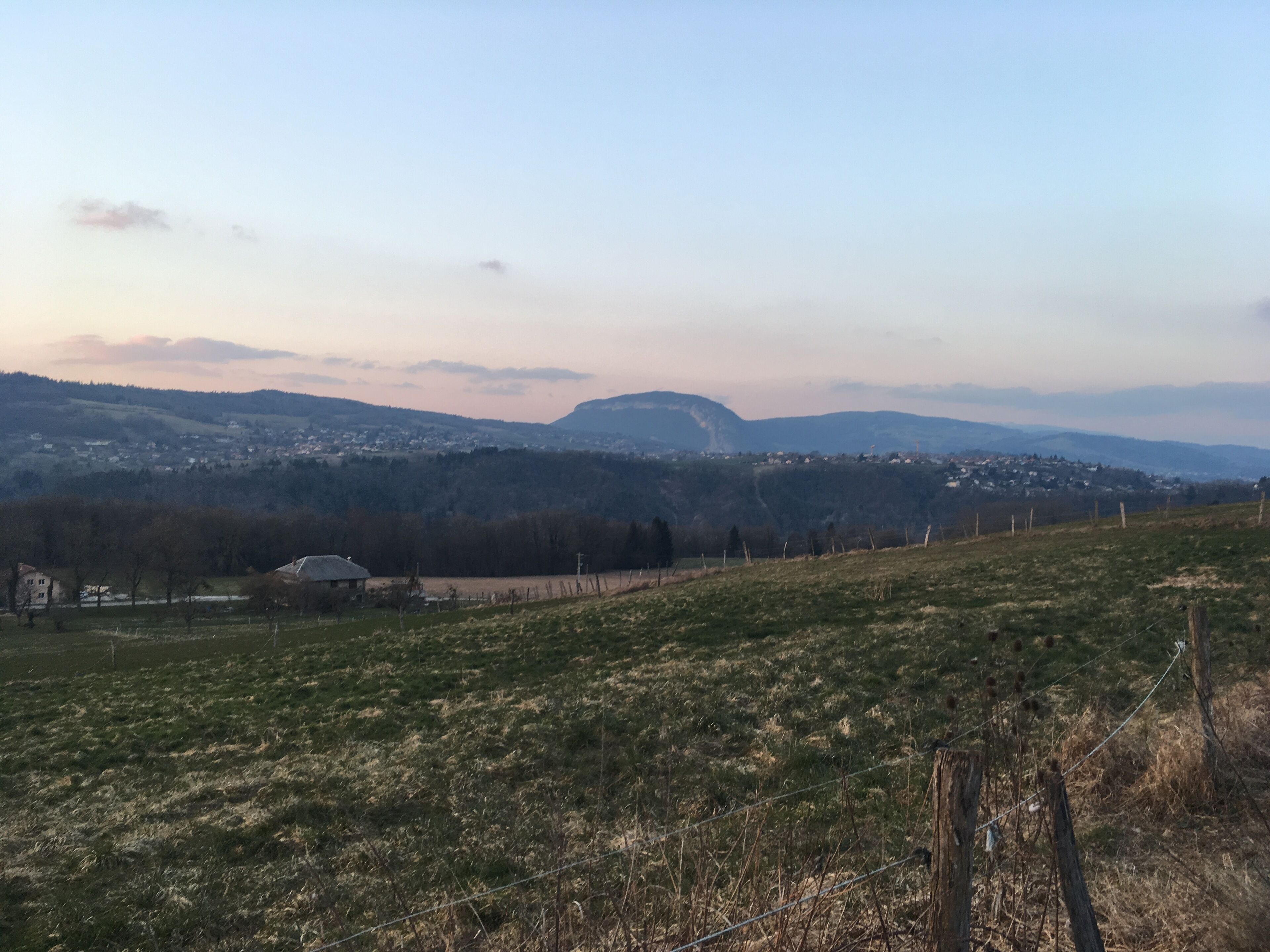 A rural landscape with rolling hills, a few scattered houses, and a distant mountain range.