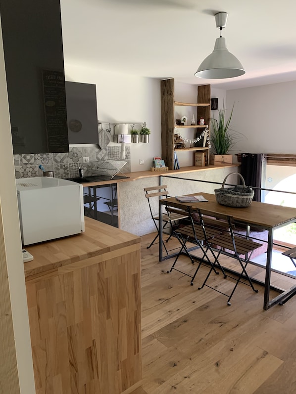 A modern kitchen with a wooden island, a dining area with a table and chairs, and a large window providing natural light. - Small independent apartment in farmhouse with air conditioning (Chavanod)