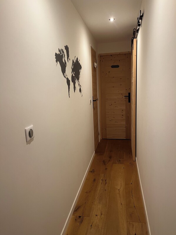 A narrow hallway with wooden flooring, a white wall with a world map decal, and a wooden door at the end. - Small independent apartment in farmhouse with air conditioning (Chavanod)