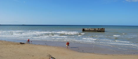 A beach with a wooden pier extending into the water, sandy shore, and people walking along the beach.