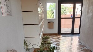 A hallway with a tiled floor, potted plants, a wooden sculpture, and a door leading outside. - Gruissan (Aude). Quiet apartment with marina view and parking space (Gruissan)