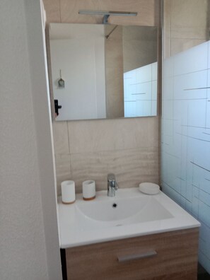 Une salle de bain avec un lavabo blanc, un miroir et deux rouleaux de papier toilette.