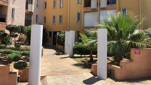 A courtyard with a central pathway flanked by white pillars, surrounded by greenery and a building with balconies and windows. - Gruissan (Aude). Quiet apartment with marina view and parking space (Gruissan)