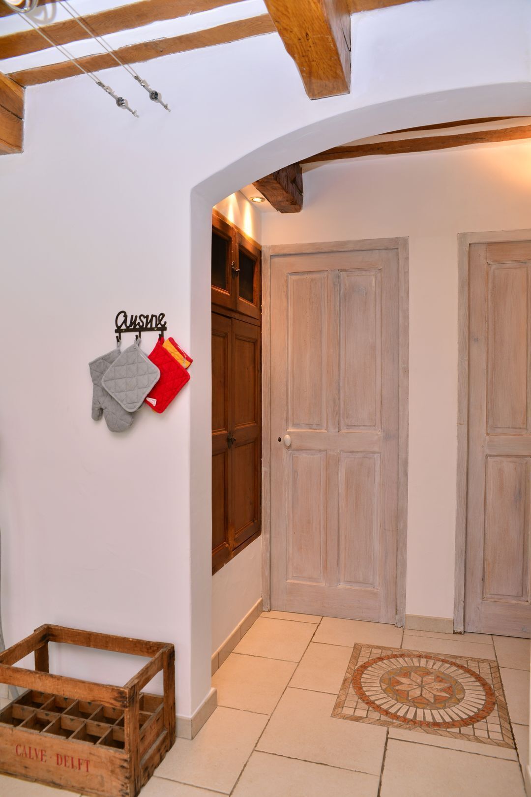 Ein Flur mit einer Holztür, einem an der Wand befestigten Handtuchhalter mit Küchentüchern und einem gefliesten Boden mit dekorativer Bordüre.