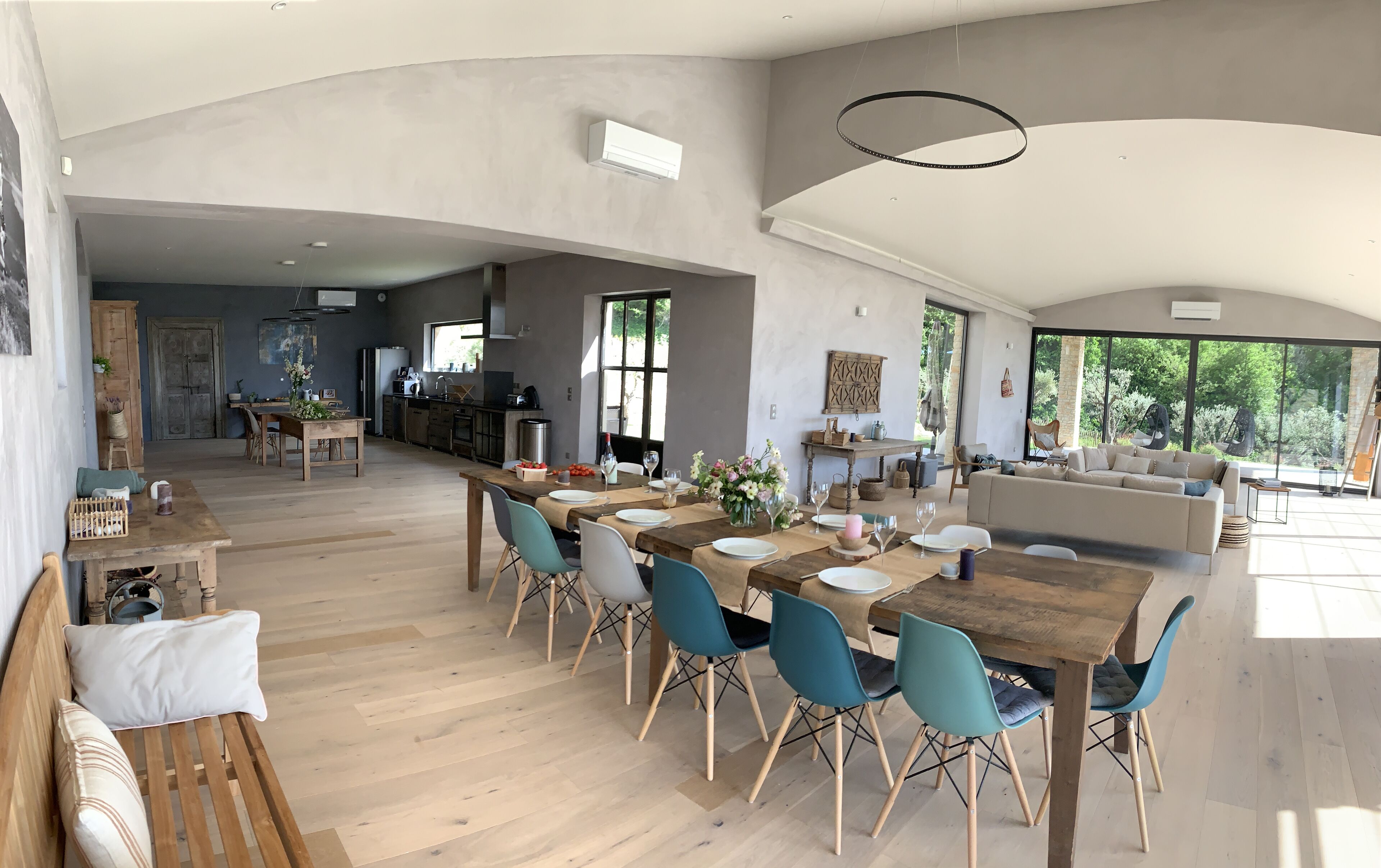 Un vaste espace dédié à la salle à manger, avec une longue table en bois, des chaises bleues et une cuisine en arrière-plan.