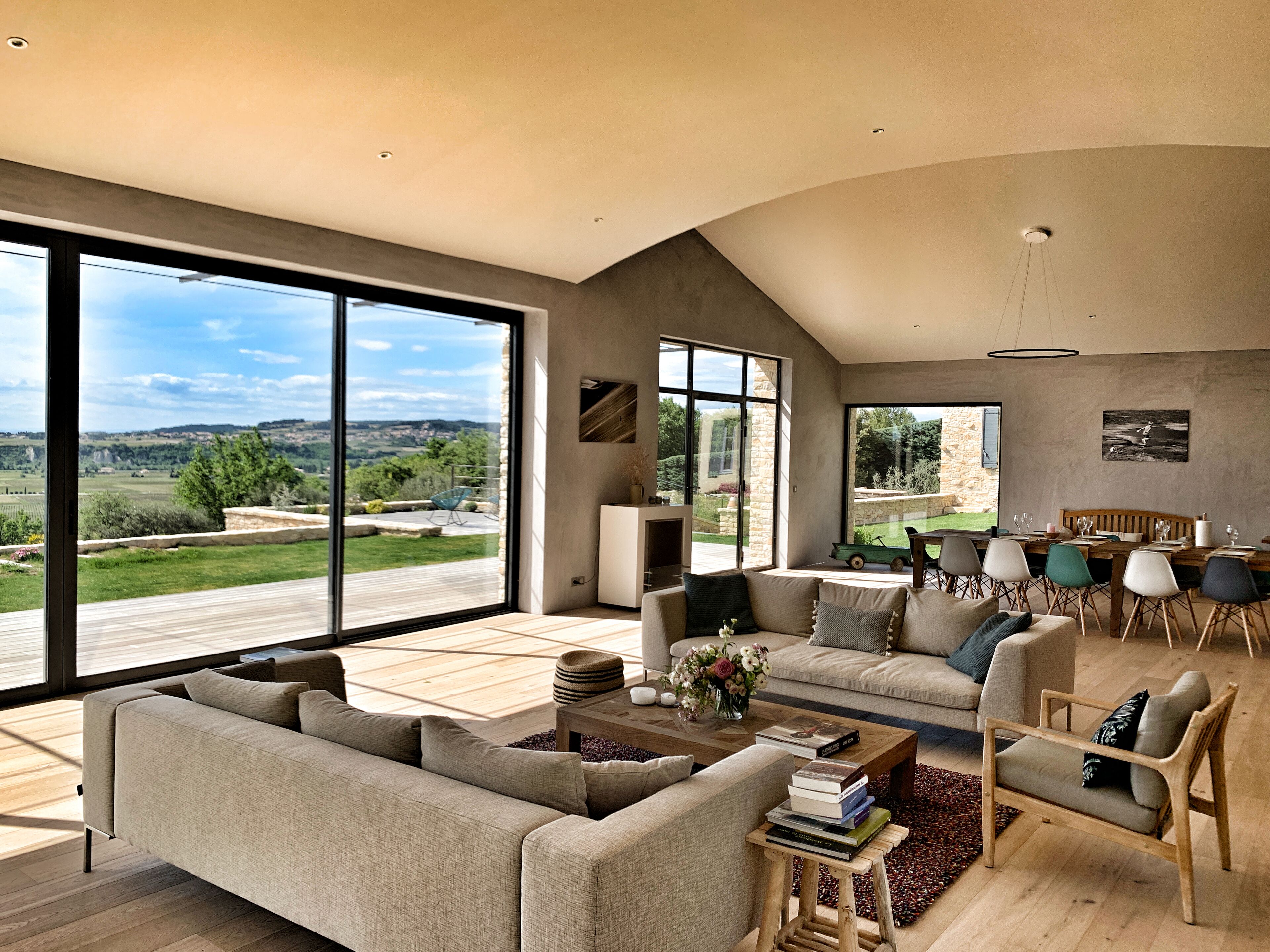 A spacious living room with large windows, a wooden deck, and a dining area with modern furniture.