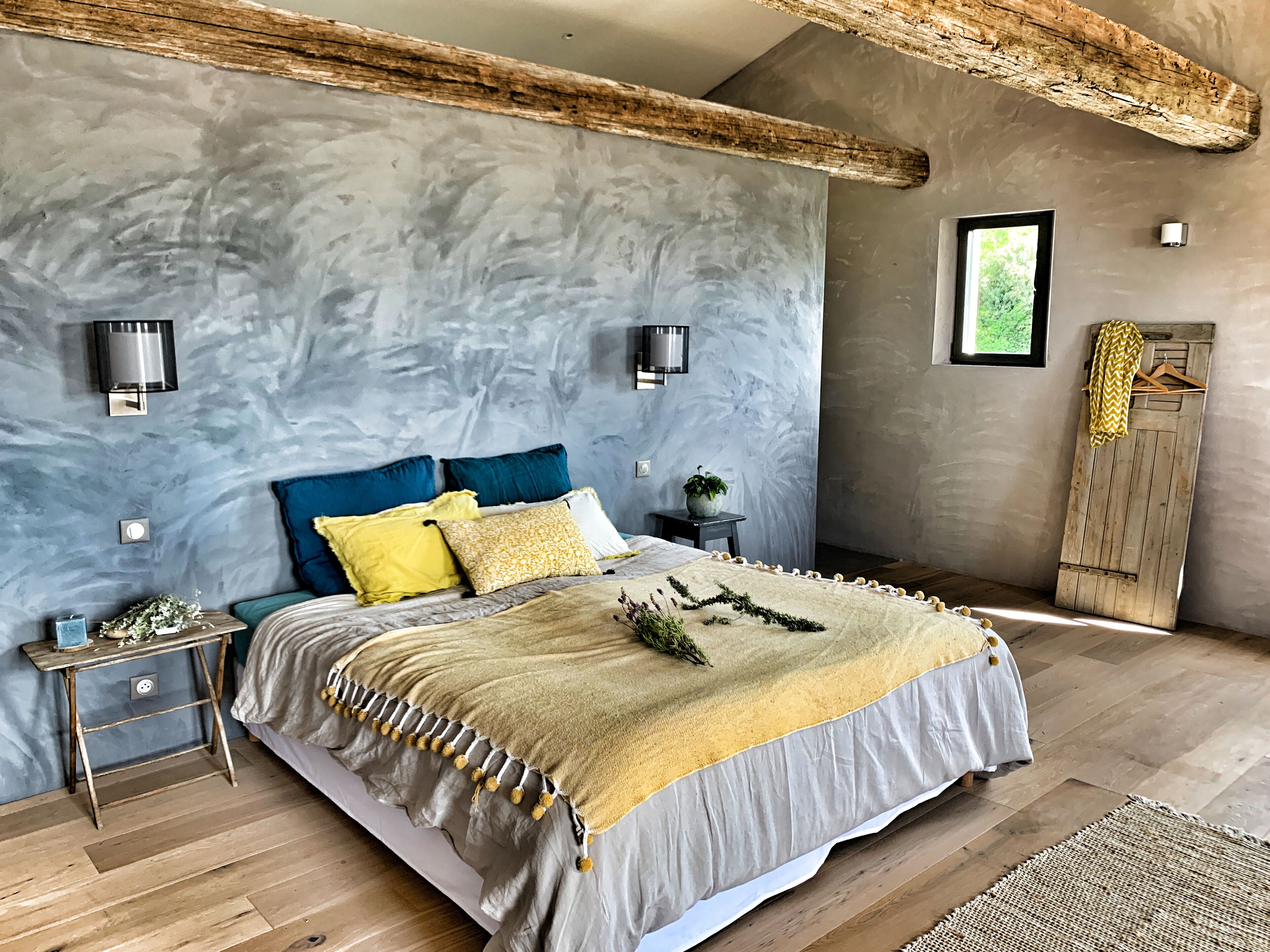 Un dormitorio con cama, mesitas de noche, luces de pared, una planta colgante y un armario de madera.