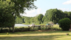 Eine grüne Wiese mit einem See, Bäumen und einem kleinen Gebäude.