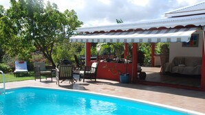 Una piscina con un porche cubierto, mobiliario exterior y un edificio rojo y blanco.