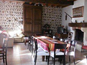 Un espace repas comprenant une longue table, des chaises, un canapé et un mur en pierre.