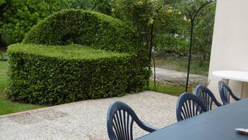 Un espace patio aménagé avec une table et des chaises, entouré d’un arbuste taillé avec soin et d’arbres.