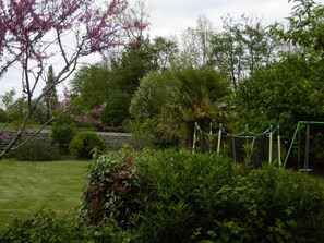 Un jardin avec différentes sortes de plantes et un ensemble de jeux avec une balançoire.