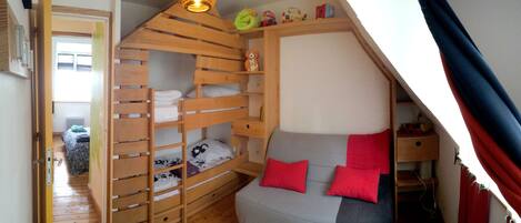 A dormitory-style room with bunk beds, a sofa with red cushions, and a small shelf with toys.