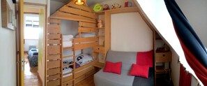 Une chambre de type dortoir avec des lits superposés, un canapé aux coussins rouges et une petite étagère avec des jouets.