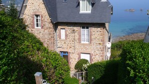 A stone house with a dark roof, a chimney, and a view of the sea. - Superb comfortable apartment with sea view (Perros-Guirec)