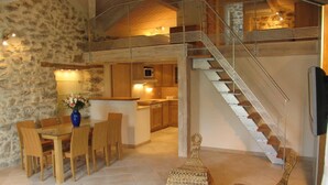 A spacious living area with a dining table and chairs, a kitchen in the background, and a staircase with a patterned railing.