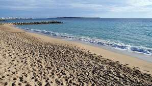 A sandy beach with footprints leading to the water, a rocky breakwater, and a distant island.