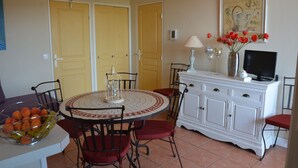 Een eetgedeelte met een ronde tafel, stoelen, een witte kast en een schilderij aan de muur.